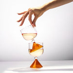 Two glasses filled with a yellowish liquid, one being poured into the other against a white background.