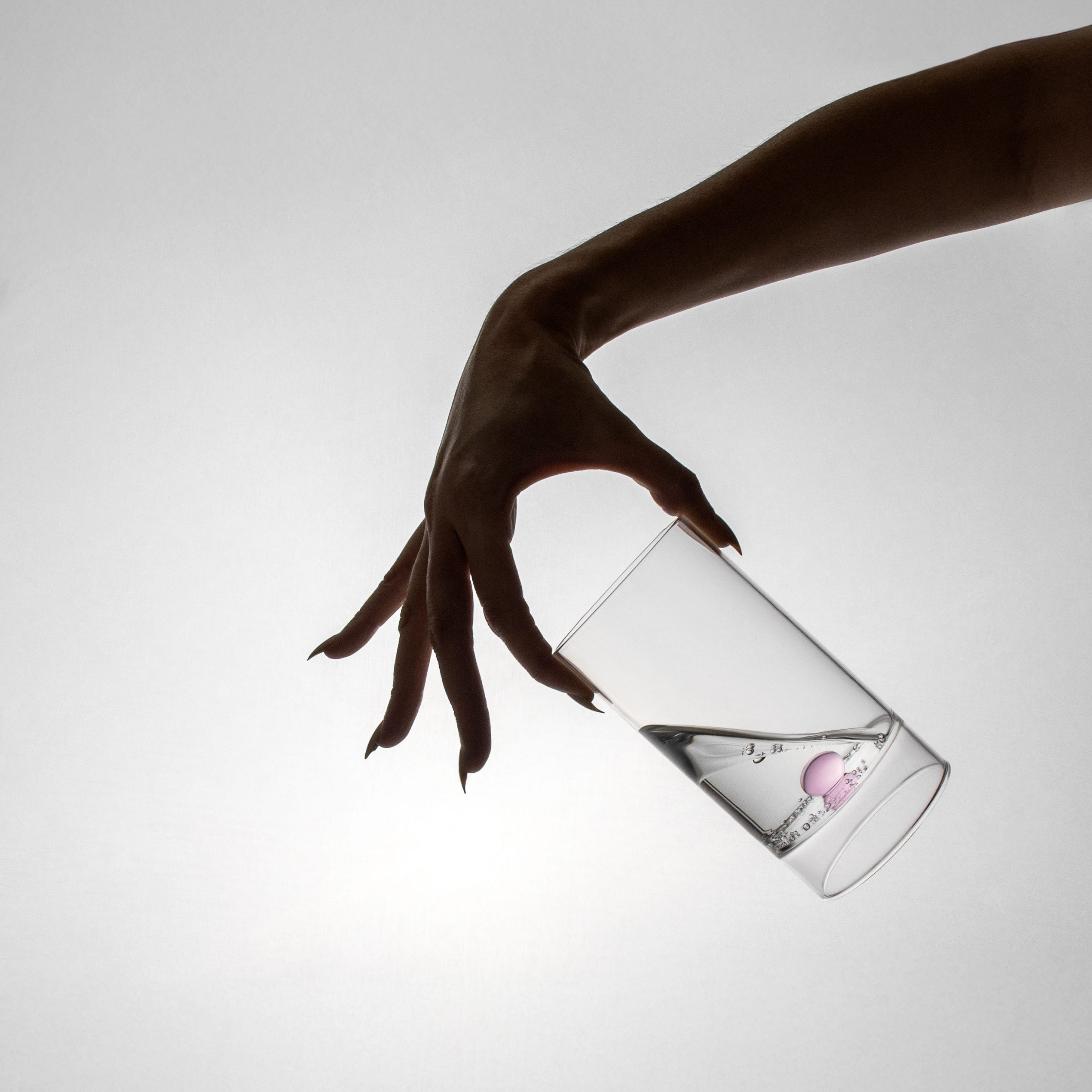 Hand holding a clear bottle with a pink label against a light gray background
